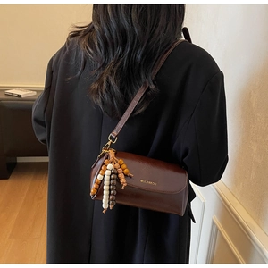 Detail view of a vintage dark brown leather cylinder bag with colorful beaded tassel decor