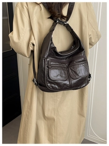 Detail view of dark coffee leather texture and silver hardware on a multi-pocket backpack