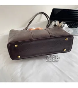 Detail view of gold protective metal studs on the bottom of a brown vintage leather tote bag