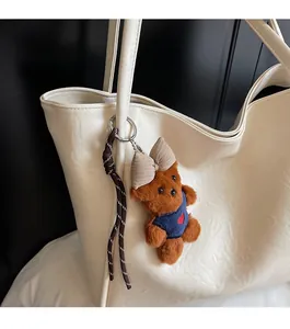 Close-up of cute brown teddy bear plush charm with a blue heart sweater on a beige tote bag