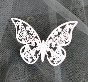 Laser-cut white paper butterfly with intricate floral lace patterns on gray mesh