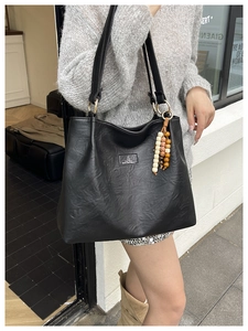 Close-up of black leather tote bag featuring golden logo and wooden bead tassel detail