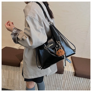 Détail du sac noir brillant avec logo doré et porte-clés ours en peluche marron