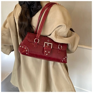 Detail of red patent leather shoulder bag with silver buckle and rivets on beige coat