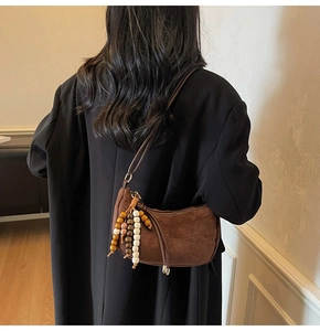 Detail of dark brown suede half-moon bag with colorful wooden bead charm on shoulder strap
