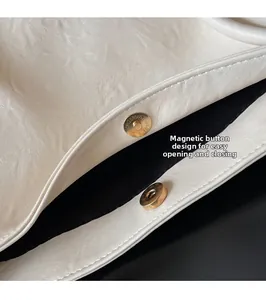 Macro detail of golden magnetic snap button on off-white leather tote bag closure