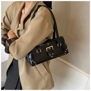 Detail of black wrinkled patent leather shoulder bag with silver rivets and metal buckle