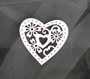 Detailed close-up of white laser-cut pearlescent paper heart with intricate floral patterns