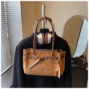 Detail of a brown suede tote bag featuring decorative wooden beads and smooth leather handles