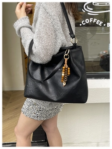 Detailed view of black faux leather tote bag with colorful wooden bead pendant detail