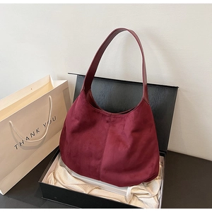 Detail view of a burgundy suede hobo bag inside a black gift box with white satin