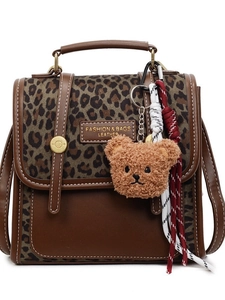 Retro brown leather handbag with leopard print and plush bear charm on white background
