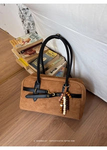 Detailed view of a brown suede Boston bag with leather straps and decorative wooden beads