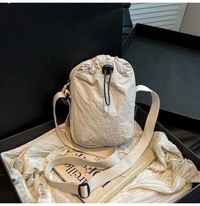 Detailed shot of cream drawstring crossbody bag with pleated texture and adjustable strap