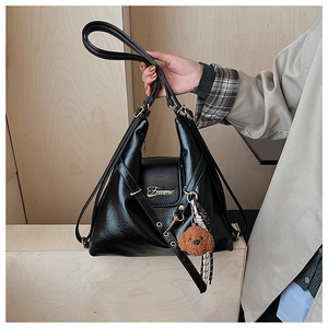 Détail du sac cabas en simili cuir noir avec logo doré, breloque ours et foulard à carreaux