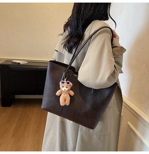 Brown vintage faux leather tote bag shown on shoulder with cute plush bear pendant
