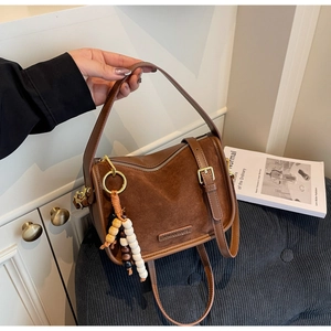 Détail d'un sac à main marron en daim mat avec pompon en perles de bois et fermeture éclair