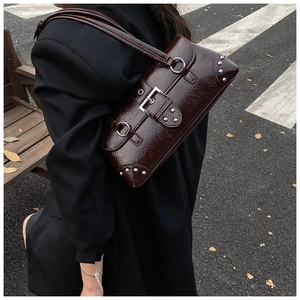 Outdoor street view of a dark burgundy patent leather shoulder bag with silver rivet details