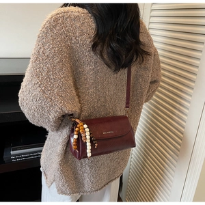 Detailed view of vintage dark red PU leather crossbody bag with beaded charm and logo