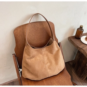 Detail of camel brown suede tote bag with vertical stitching on a vintage wooden chair