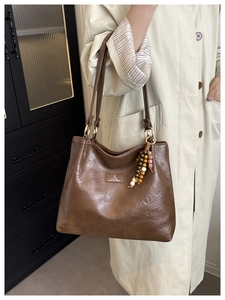 Detail of a large brown leather tote bag with a boho bead charm and logo patch