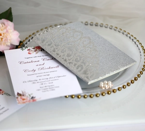 Dettaglio dell'invito di nozze tagliato al laser con glitter argento e fiori rosa