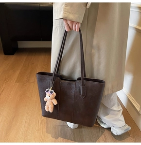 Detail of dark brown leather tote bag with a cute bear charm and vintage texture