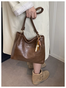 Detail of a brown faux leather tote with vintage texture and colorful wooden bead charm