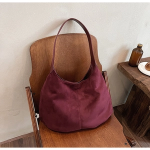 Close-up of burgundy suede tote bag resting on a wooden chair in a minimalist home setting