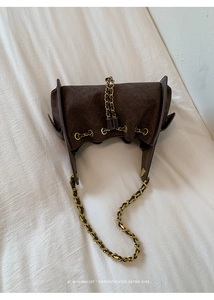 Détail d'un sac à main en daim matelassé marron foncé avec chaîne dorée et cordon de serrage