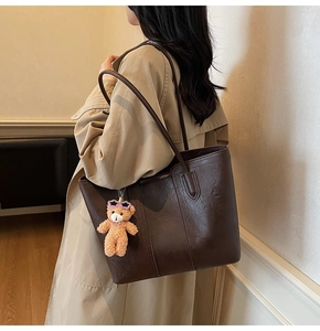 Detail of dark brown tote bag with vintage texture and plush bear charm on model