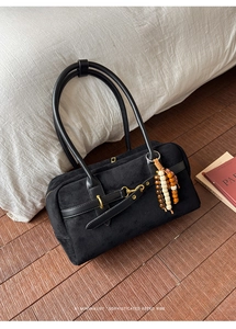 Detail of black suede Boston bag with leather handles and decorative colorful beaded tassel