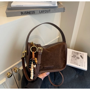 Détail du sac bandoulière en daim marron avec boucles dorées et breloque en perles de bois