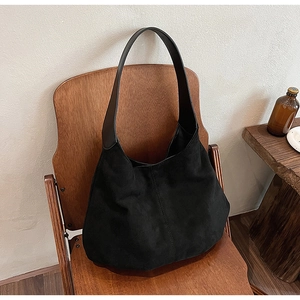 Detailed view of a black suede tote bag placed on a vintage wooden folding chair