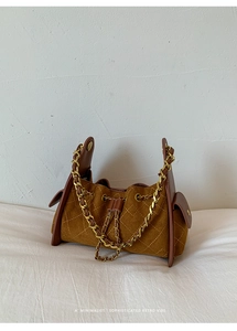 Gros plan du sac seau en daim matelassé marron avec chaîne dorée et détails en cuir