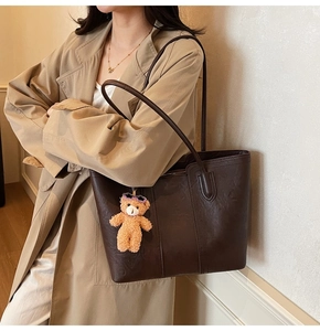 Detail of dark brown large tote bag with plush bear charm on beige trench coat outfit