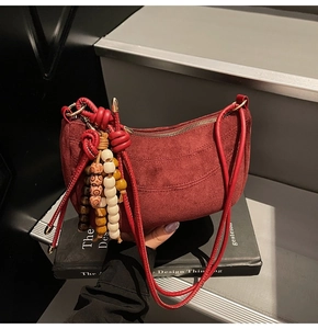 Close-up of matte suede hobo bag in burgundy with decorative beaded tassel and thin strap