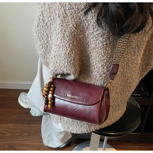 Detail of dark red leather crossbody bag with ethnic woven strap and beaded charm