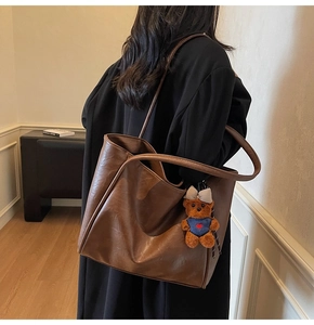 Brown leather tote bag featuring a cute teddy bear charm shown from a back carry view