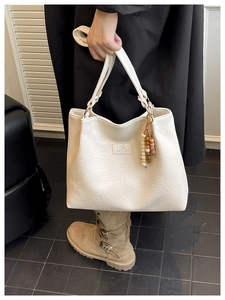 Detail of creamy white textured tote bag featuring vintage pleats and beaded charms