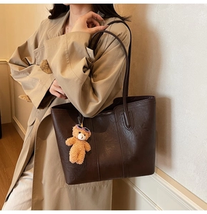 Detail of a dark brown vintage tote bag with high-quality leather texture and a bear charm