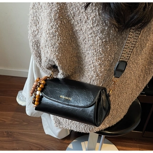 Detail of vintage black leather cylinder bag with wide woven strap and wood bead charm