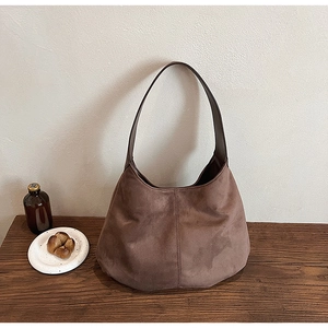 Detail of dark brown suede tote bag with leather shoulder strap on a wooden table