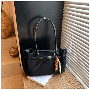 Detail of black frosted tote bag with wooden bead charm and sleek leather handles