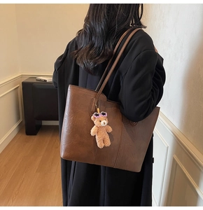 Detail view of large dark brown leather tote bag with stylish plush bear charm