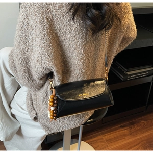 Close-up of black leather crossbody bag with decorative wooden beads on a knit sweater