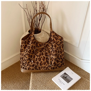Detail of leopard print tote bag with brown faux leather trim and decorative bow on rug