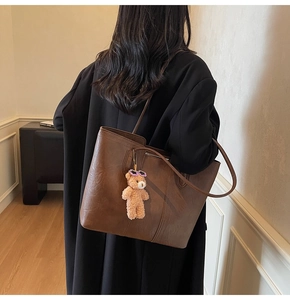 Detail of dark brown leather tote bag with a purple sunglasses bear plush charm accessory