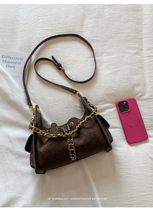 Détail de la texture du sac en daim marron foncé avec matelassage et chaîne dorée