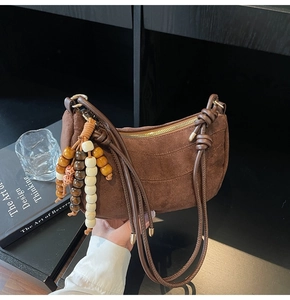 Detail of brown suede shoulder bag featuring a beaded tassel and gold zipper hardware